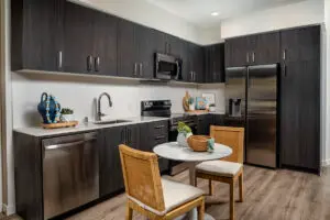 Model kitchen at Alta Merita Apartments in Rancho Cucamonga, featuring stainless steel appliances and a dining table.